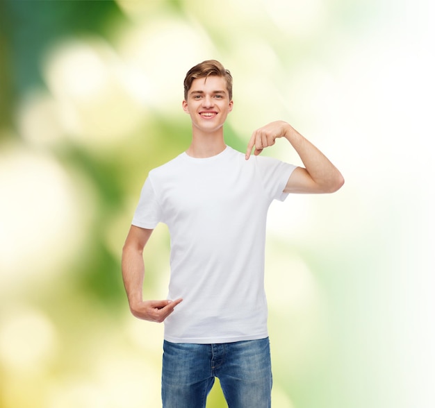 gesto, publicidad, ecología y concepto de la gente - joven sonriente con una camiseta blanca en blanco apuntándose con el dedo sobre el fondo verde