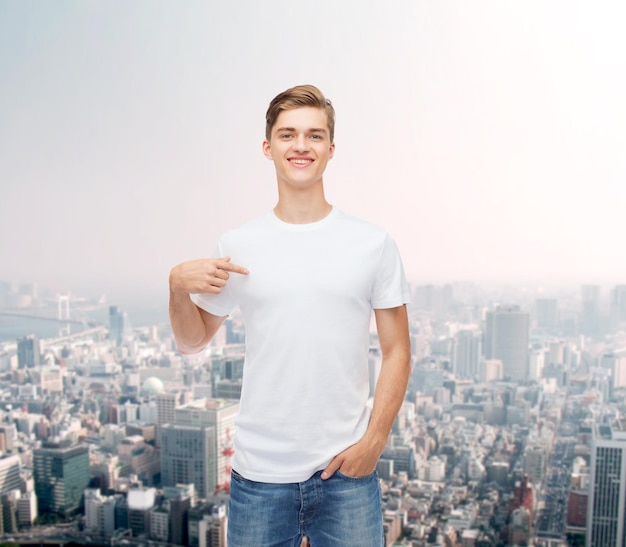 gesto, publicidade e conceito de pessoas - jovem sorridente em camiseta branca em branco apontando o dedo sobre si mesmo sobre o fundo da cidade