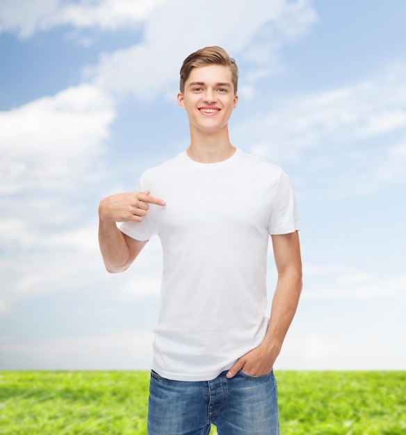 gesto, publicidade, férias de verão e conceito de pessoas - jovem sorridente em camiseta branca em branco apontando o dedo sobre si mesmo sobre fundo natural