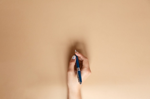 Gesto y signo, mano femenina sosteniendo un bolígrafo azul metálico y escribiendo en marrón, plano