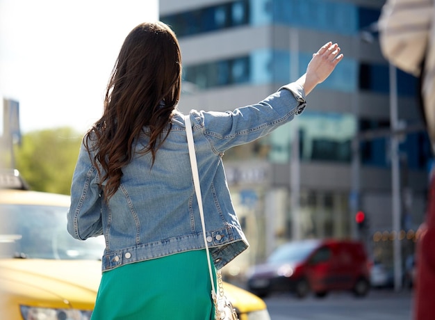 Foto gesto, transporte, viajes, turismo y concepto de personas - mujer joven o adolescente cogiendo un taxi en la calle de la ciudad o haciendo autostop