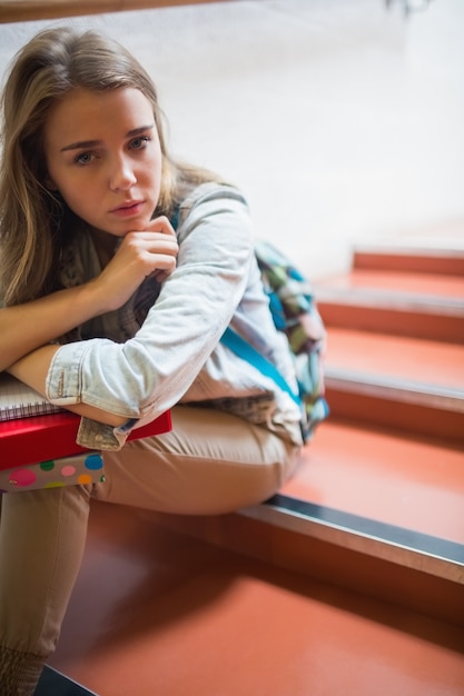 Gestörter einsamer Student, der auf der Treppe betrachtet Kamera sitzt