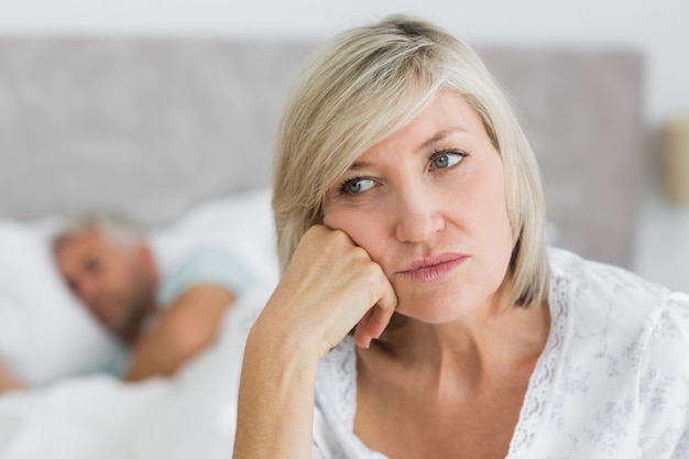 Gestraffte reife Frau, die im Bett mit Mann im Hintergrund sitzt