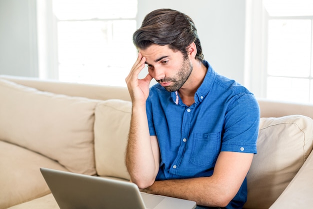 Gestraffter Mann, der im Laptop beim Sitzen auf Sofa schaut