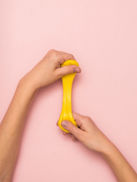Gestrecktes Stück gelber Schleim in den Händen auf rosafarbenem Hintergrund. Spielzeug gegen Stress. Spielzeug zur Entwicklung der Handmotorik.
