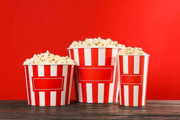 Gestreifte Eimer mit Popcorn gegen roten Hintergrund