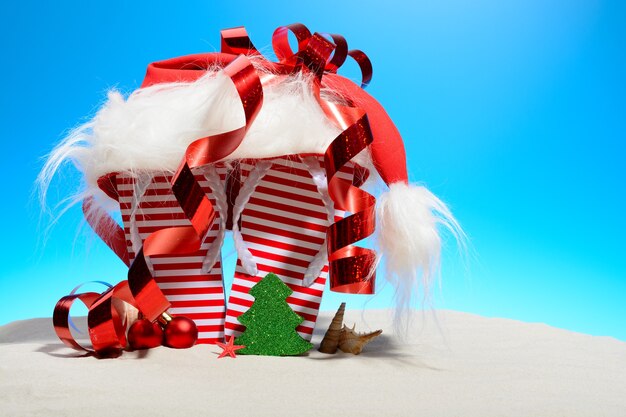 Gestreifte Flip-Flops und Weihnachtsmütze am tropischen Strand, stehend auf dem Sand gegen einen sonnigen blauen Himmel mit Kopienraum