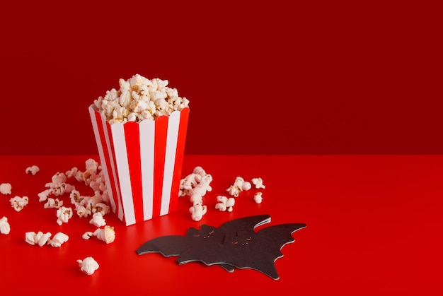 Gestreifte Schachtel mit Popcorn-Fledermaus-Serviette auf rotem Hintergrund