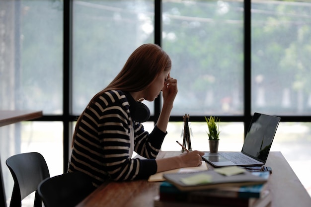 Gestresste asiatische Frau bedeckt ihr Gesicht mit der Hand und fühlt sich verärgert von der Arbeit vor dem Laptop auf dem Schreibtisch im BüroStress-Büro-Lifestyle-Konzept