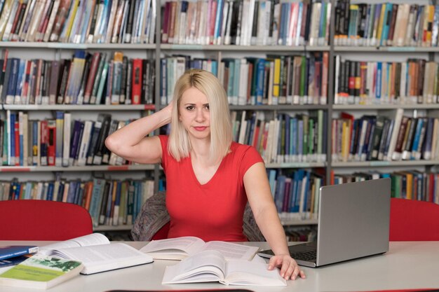 Gestresste junge Studentin, die Lehrbuch liest, während sie in der Bibliothek sitzt