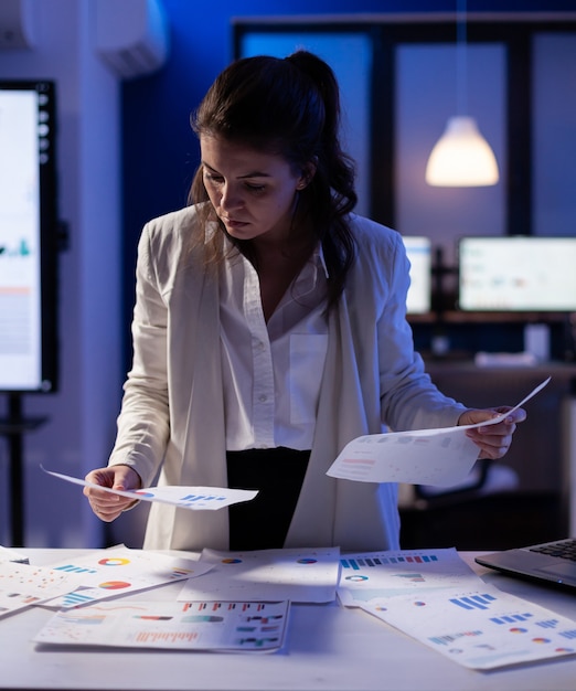 Gestresste Managerin, die mit Finanzdokumenten arbeitet, Diagramme überprüft, Papiere bis spät in die Nacht hält