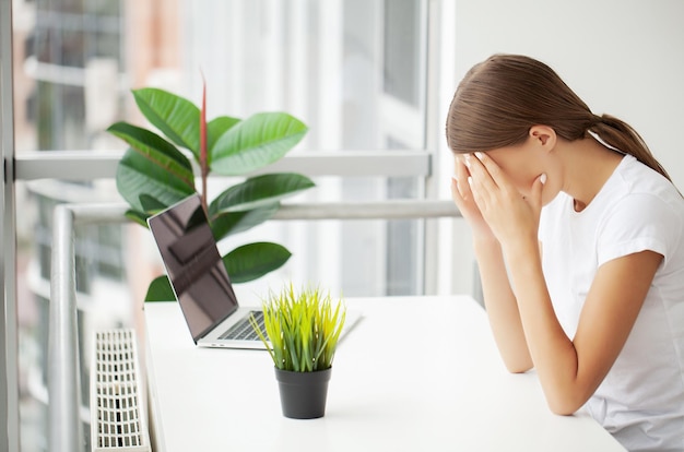 Gestresster junger Büroangestellter, der wegen Schmerzen im Büro den Kopf hält