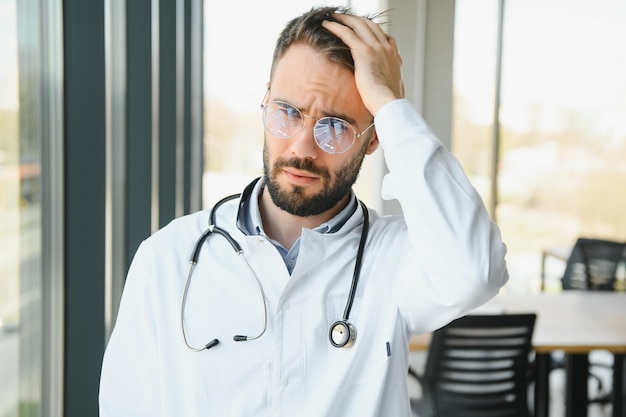 Gestresster männlicher Arzt Mittlerer erwachsener männlicher Arzt, der viele Stunden arbeitet Überarbeiteter Arzt in seiner Praxis Nicht einmal Ärzte sind von Burnout ausgenommen