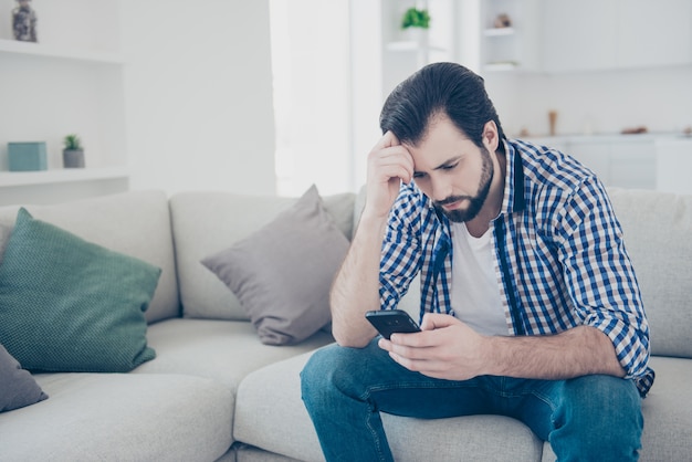 Gestresster Mann zu Hause auf Sofa mit Smartphone