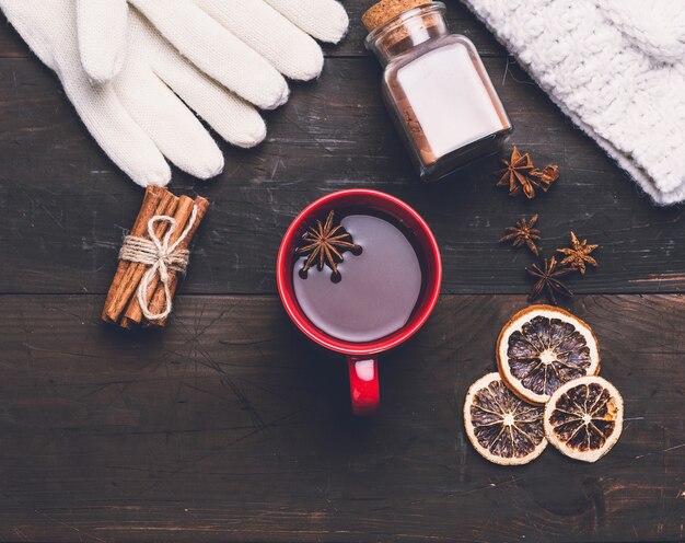 Gestrickte Handschuhe und rote Tasse mit einem Getränk auf braunem Holztisch, Draufsicht