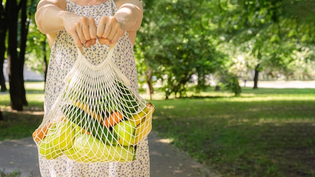 Gestrickte Netztasche mit Gemüse und Obst in den Händen einer Frau