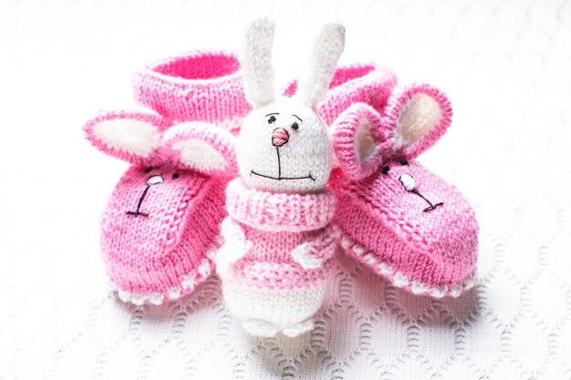 Gestrickte rosa Babyschuhe mit Hasenmaulkorb und Spielzeug über Textilhintergrund