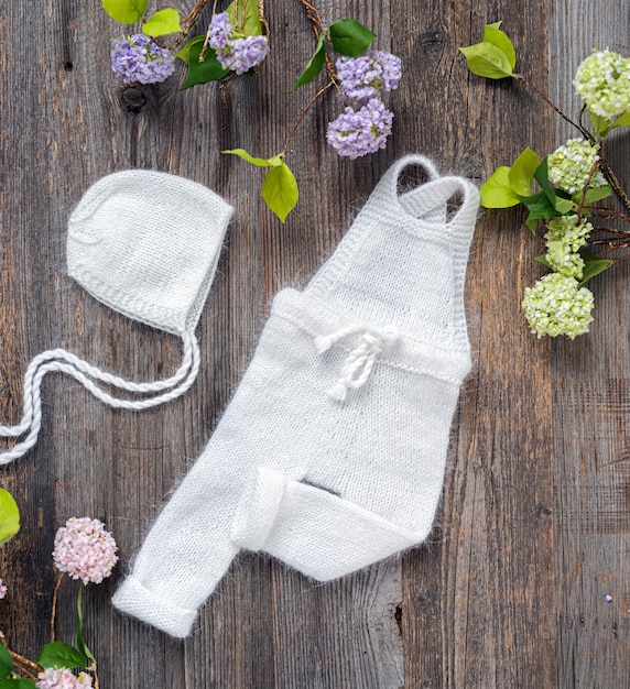 Gestrickte weiße Kleidungszusammensetzung für Neugeborene auf dem Holztisch