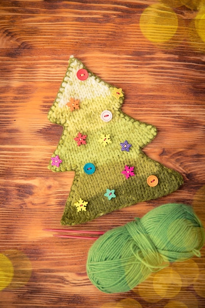 Gestrickter Weihnachtsbaum mit Knöpfen auf Holzhintergrund. Weihnachtsferienkonzept