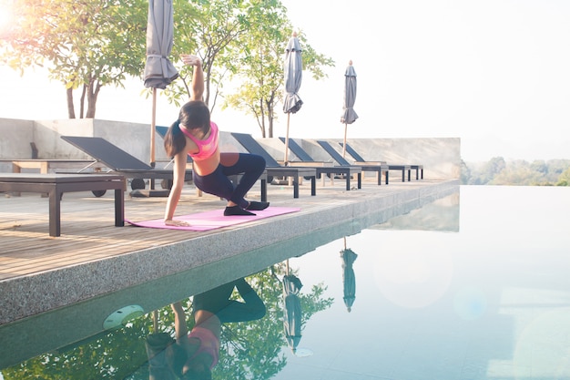 Gesunde asiatische Frau, die Yoga tut und nahe Swimmingpool trainiert. Gesund und Wohlbefinden