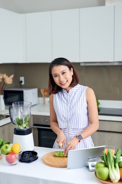 Gesunde asiatische Frau genießt es, grünes Gemüse zu entgiften und grünen Frucht-Smoothie mit Mixer in der Küche zu Hause zu machen. Diätkonzept.gesunde Lebensweise