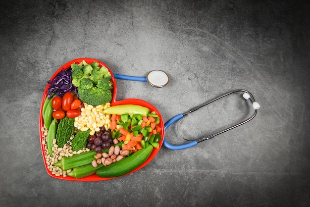 Gesunde Auswahl von Lebensmitteln sauberes Essen für Herz Leben Cholesterin Diät Gesundheit Frischer Salat Obst und Gemüse gemischt verschiedene Bohnen Nüsse Korn auf rotem Herz Teller für gesundes Essen vegan kochen