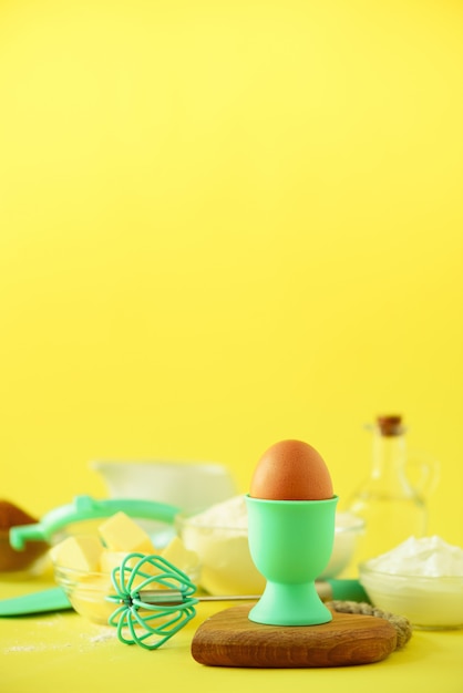 Gesunde Backzutaten - Butter, Zucker, Mehl, Eier, Öl, Löffel, Pinsel, Schneebesen, Milch über gelbem Hintergrund.