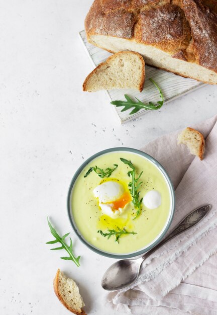 Gesunde Blumenkohlsuppe mit pochiertem Ei, Olivenöl und Rucola in einer Keramikschale