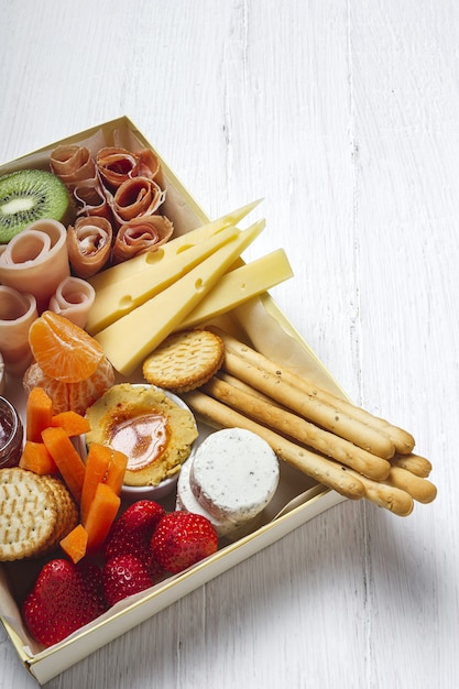 Gesunde Brunchbox zum Mitnehmen mit Schinken, Erdbeeren; Kiwi; Brot; Kekse; Käse, Karotten, Mandarinen, Hummus.