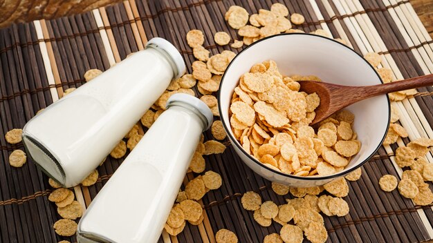 Gesunde Cornflakes und Milch und ein Holzlöffel auf einer Bambusserviette. Glasflaschen mit Milch für ein gesundes Frühstück