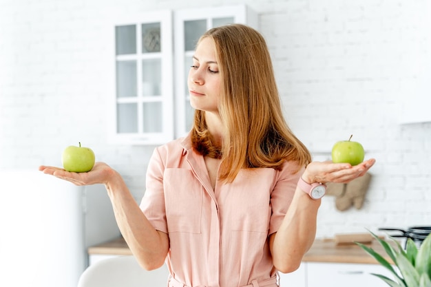 Gesunde Diätfrucht in den Händen der hübschen Frau. Junge vegetarische Dame, die auf grünem reifer Apfel schaut.