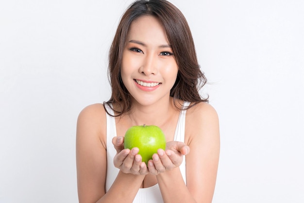 Gesunde Ernährung der schönen asiatischen jungen Frau, die weiße Unterwäsche trägt, die grünen Apfel mit der gesunden Nahrung lokalisiert auf einem weißen Hintergrund hält