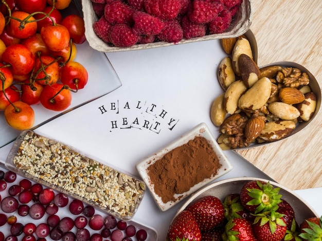 Foto gesunde ernährung für das herz-kreislauf-system mit holzform aus herz samen himbeeren erdbeeren preiselbeeren kirschnüsse kakao antioxidantien reiche nahrung