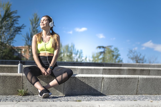 Foto gesunde frau, die sich ausruht und musik mit dem handy hört, während sie yoga und training macht