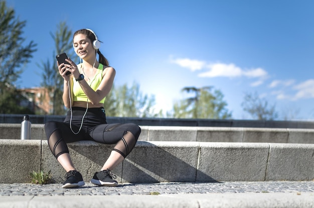 Foto gesunde frau, die sich ausruht und musik mit dem handy hört, während sie yoga und training macht