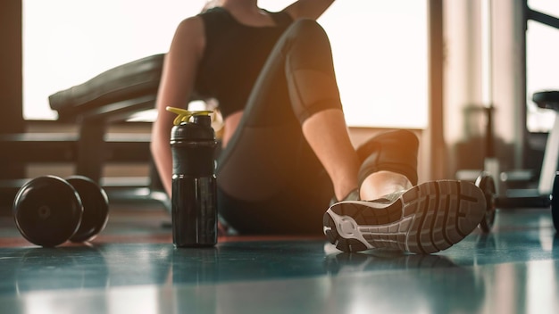 Gesunde Frauen sitzen und entspannen sich nach dem Training mit Molkenprotein nach dem Training im Indoor-Fitnessstudio.