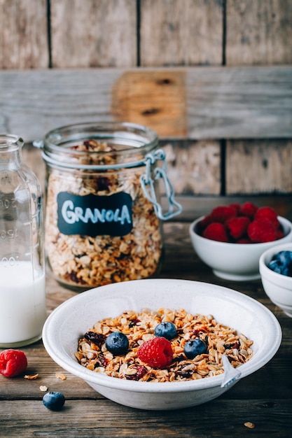 Gesunde Frühstücksschüssel Hausgemachtes Müsli mit Naturjoghurt Blaubeeren und Himbeeren auf einem hölzernen rustikalen Hintergrund