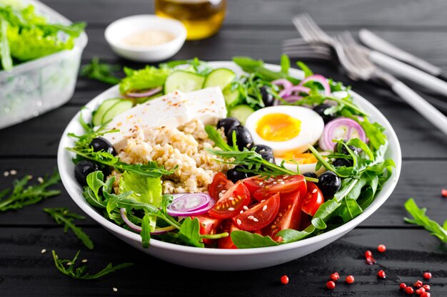 Gesunde Frühstücksschüssel im griechischen Stil mit Haferbrei und frischem Gemüsesalat aus Kopfsalat, Rucola, Oliven, Tomaten, Gurken, Feta-Käse und gekochtem Ei