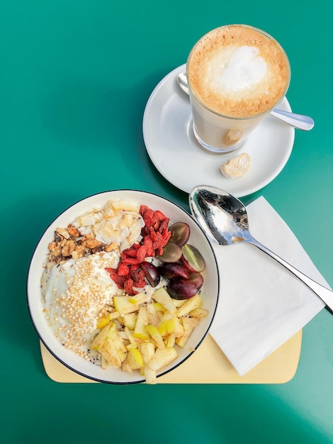 Gesunde Frühstücksschüssel mit frischem Obst und flachem weißem Kaffee