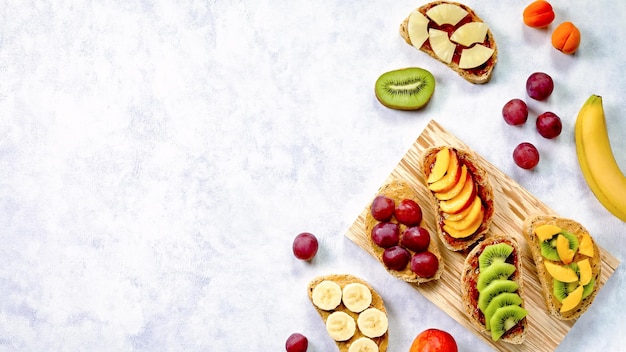 Gesunde Frühstückstoasts mit Erdnussbutter, Erdbeermarmelade, Bananentrauben, Pfirsich, Kiwi, Ananas, Nüssen. Kopieren Sie Platz