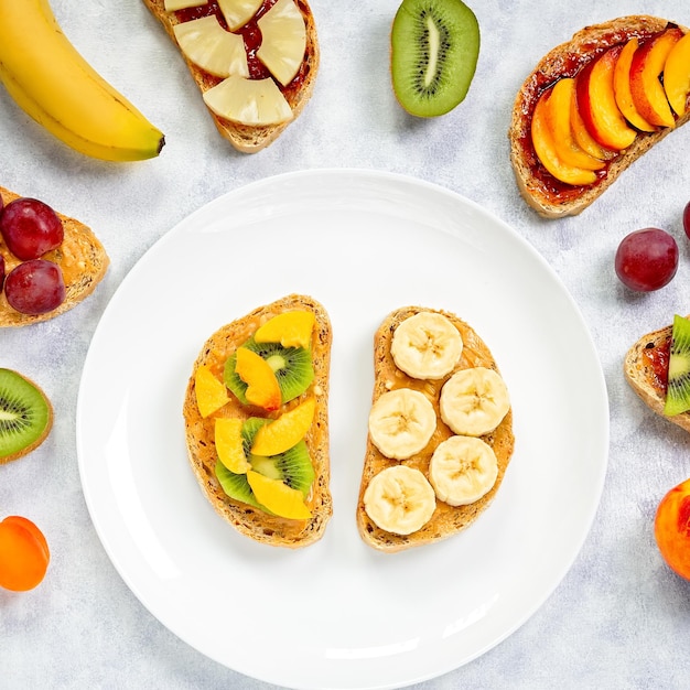 Gesunde Frühstückstoasts mit Erdnussbutter, Erdbeermarmelade, Bananentrauben, Pfirsich, Kiwi, Ananas, Nüssen. Kopieren Sie Platz