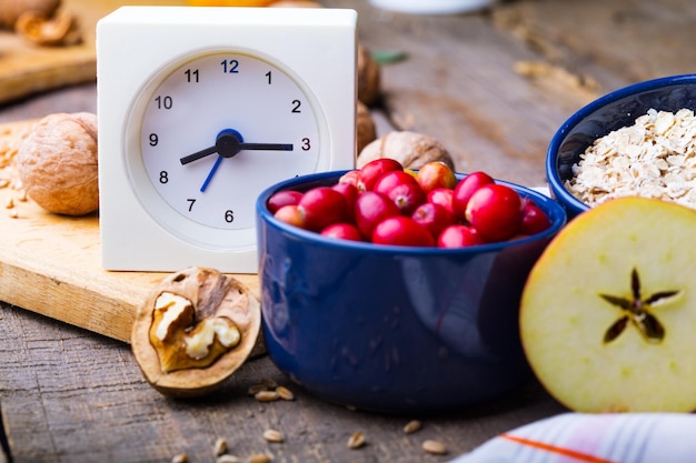 Gesunde Frühstücksuhr Milch Haferflocken Preiselbeeren Nüsse Äpfel auf einem Holztisch xA