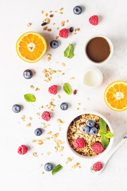 Gesunde Frühstückszutaten: Müsli mit Milch, Beeren (Heidelbeere und Himbeere), Orange und Milch.