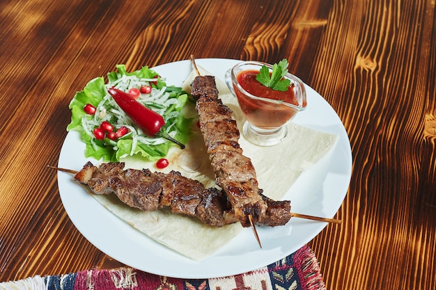 Gesunde gegrillte magere gewürfelte Schweinefleischspiesse, serviert mit einer Maistortilla und frischem Salat- und Tomatensalat, Nahaufnahme