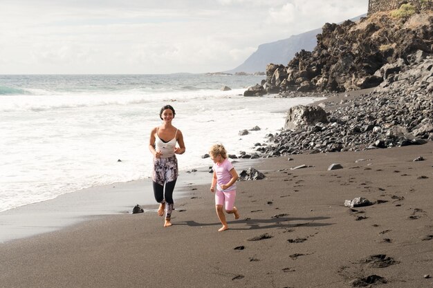 Gesunde, glückliche Familienmutter und -tochter, die Dehnübungen am Meer machen