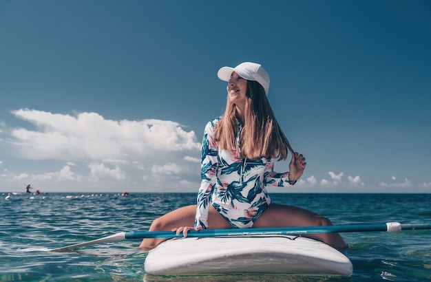 Gesunde, glückliche, fitte Frau im Bikini, die sich auf einem SUP-Surfbrett entspannt, das auf dem klaren türkisfarbenen Meer schwimmt?