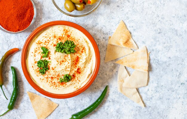 Gesunde hausgemachte Hummus serviert mit Paprikapulver, Fladenbrot, Oliven und Petersilie. Nahöstliche Küche, israelische Küche, levanesische Küche, levantinische Küche.