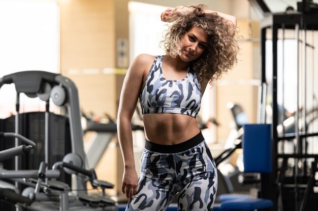 Gesunde junge Frau, die stark in der Turnhalle steht und Muskeln beugt Schönes athletisches Eignungs-Modell, das nach Übungen aufwirft