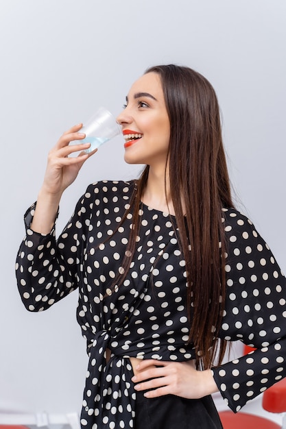 Gesunde junge Frau mit Glas Süßwasser auf weißem Hintergrund. Brünettes Mädchen mit roten Lippen und langen Haaren.