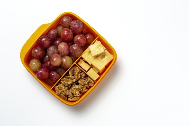 Gesunde Lebensmittel in Plastikbehältern, die mit Käse, Trauben und Walnüssen auf dem Arbeitstisch verzehrfertig sind